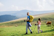 Mann mit Kind wandert auf Alm mit Rindern | © Magnific