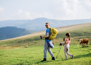 Mann mit Kind wandert auf Alm mit Rindern | © Magnific