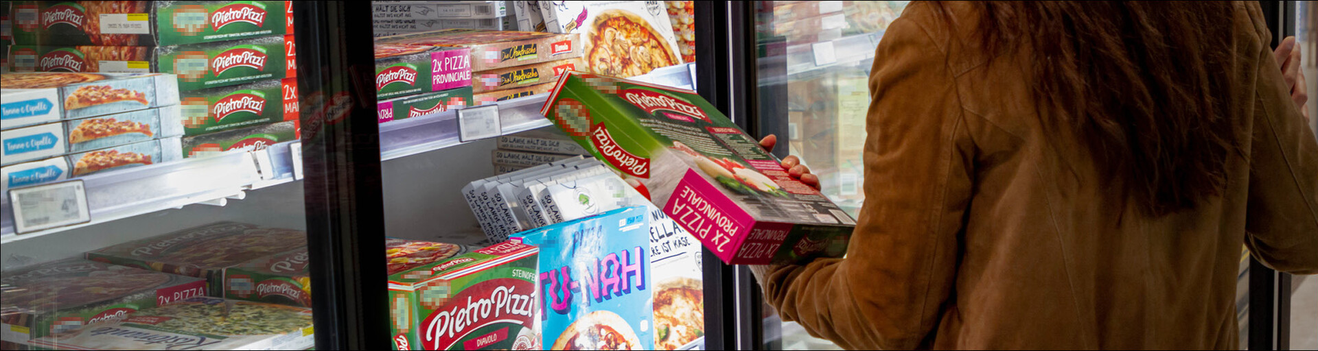 dunkelhaarige Frau vor dem Kühlregal hält eine Tiefkühlpizza in der Hand | © Land schafft Leben