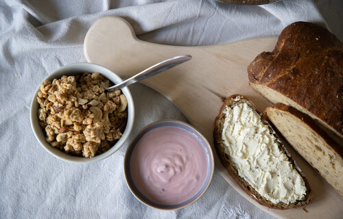 Versteckter Zucker | © Land schafft Leben Brot auf Holzbrett neben Schüssel mit Joghurt und Schüssel mit Müsli | © Land schafft Leben